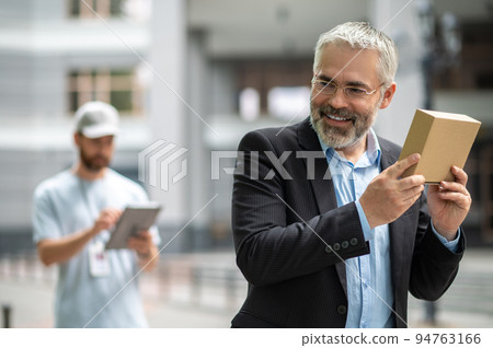 Bearded elegant businessman taking the box from a courrier Bearded elegant businessman taking the box from a courrier 94763166
