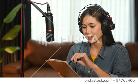 Attractive woman using microphone and laptop recording audio for her channel at small broadcast home studio Attractive woman using microphone and laptop recording audio for her channel at small broadcast home studio 94763400