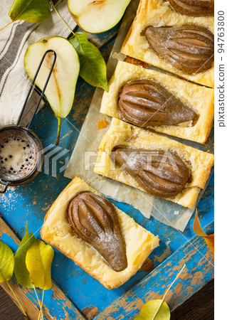 Homemade Cake Puff Pastry with Pear and Stuffed with Nut Cream a blue wooden table. Top view flat lay background. Homemade Cake Puff Pastry with Pear and Stuffed with Nut Cream a blue wooden table. Top view flat lay background. 94763800