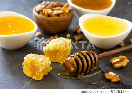 Natural Various Honey and Nuts. Honey in glass jar and dipper, Sweet Honeycombs on dark stone table. 94763884