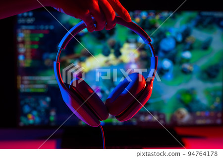 Woman holding headphones on the background of a computer game on the monitor. Woman holding headphones on the background of a computer game on the monitor. 94764178
