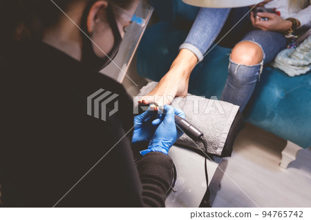 Pedicure master uses nail file drill for preparing nails for pedicure. Pedicure master uses nail file drill for preparing nails for pedicure. 94765742