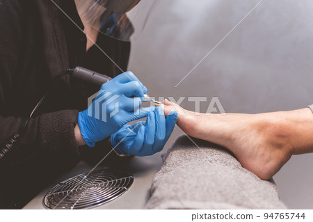 Pedicure master polishes nails with nail file drill before applying varnish side view. 94765744