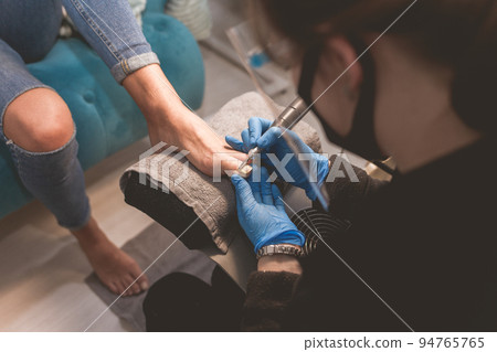 Pedicure master uses nail file drill for preparing nails for pedicure. Pedicure master uses nail file drill for preparing nails for pedicure. 94765765