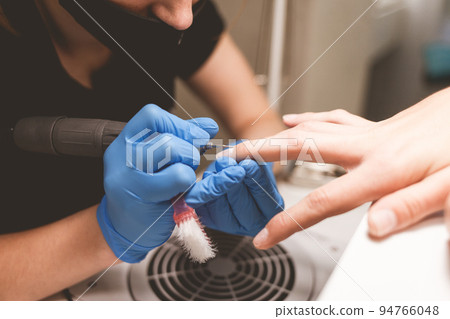 Manicurist cleans nails with a nail file drill before applying varnish. 94766048