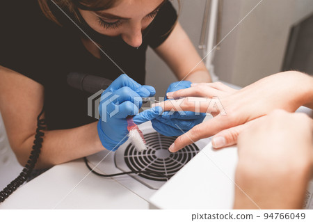 Manicurist cleans nails with a nail file drill before applying varnish. 94766049