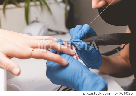 Manicurist cleans nails with a nail file drill before applying varnish. 94766050