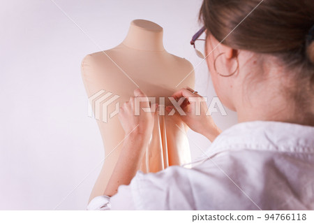 Seamstress cuts fabric with big scissors on a mannequin.. 94766118