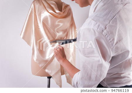 Seamstress cuts fabric with big scissors on a mannequin.. 94766119