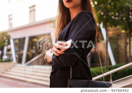 Bines lady in a stylish jacket and a bag on her shoulder holds a smartphone in her hand.. 94766492