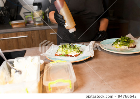 Cook hands preparing and making sandwich. Preparing healthy vegetarian bruschettas in dark gloves. Sandwich with soft cheese, arugula and cucumber.. Cook hands preparing and making sandwich. Preparing healthy vegetarian bruschettas in dark gloves. Sandwich with soft cheese, arugula and cucumber.. 94766642