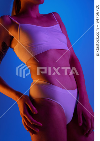 Cropped image of sportive, muscular built female body in white underwear isolated over blue studio background in neon light Cropped image of sportive, muscular built female body in white underwear isolated over blue studio background in neon light 94766720