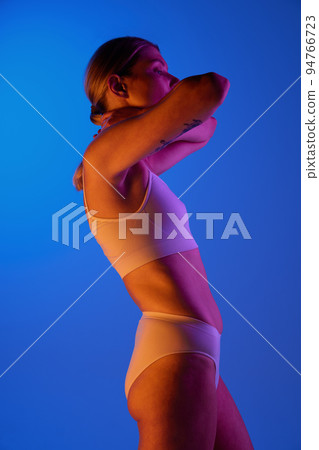 Portrait of sportive woman posing in white underwear isolated over blue background in pink neon light 94766723