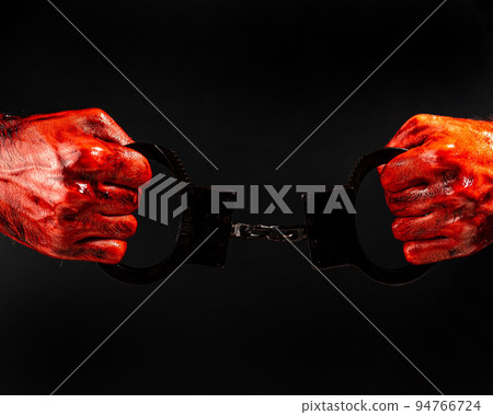 A man with bloody hands holds iron handcuffs. A man with bloody hands holds iron handcuffs. 94766724