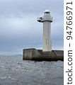 A white lighthouse standing on the breakwater and the sea 94766971