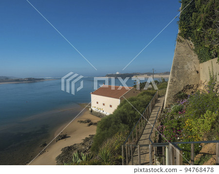 Idyllic view of the mouth of Mira river flowing into the Atlantic Ocean with stairs leading to port and ferry and small beach house. Vila Nova de Milfontes, Vicentine Coast Natural Park Portugal 94768478