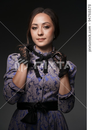 The middle plan is a portrait of a medieval young woman in a blue vintage dress with a black lace collar, posing on a dark background. Historical fashion of the 19th century. High quality photo The middle plan is a portrait of a medieval young woman in a blue vintage dress with a black lace collar, posing on a dark background. Historical fashion of the 19th century. High quality photo 94768878