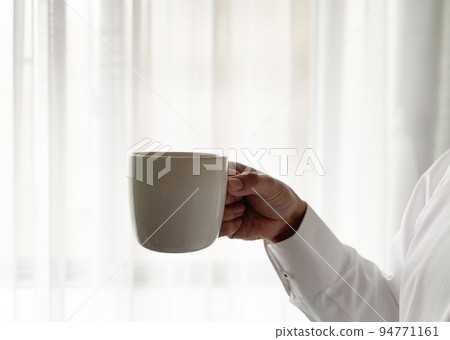 Hand of a man drinking coffee by the window Hand of a man drinking coffee by the window 94771161