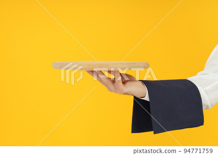 Male hand of waiter holds empty tray on yellow background 94771759