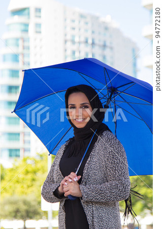 Portrait of smiling young woman holding big blue umbrella Portrait of smiling young woman holding big blue umbrella 94772180