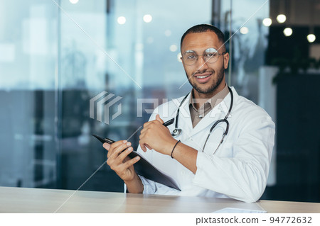 Webcam view hispanic doctor looking at camera and consulting patients man in medical gown working remotely inside modern clinic office. Webcam view hispanic doctor looking at camera and consulting patients man in medical gown working remotely inside modern clinic office. 94772632