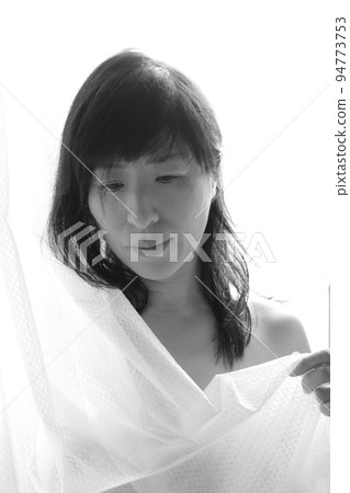 The figure of a woman holding a curtain while bathing in the morning sun 94773753