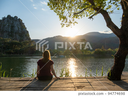 Woman relaxing outdoors near lake or river at sunset, meditating on the background of nature. Healthy lifestyle and relax concept 94774698