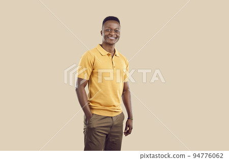 Young smiling African American man posing with one hand in pocket pants stands on beige background 94776062
