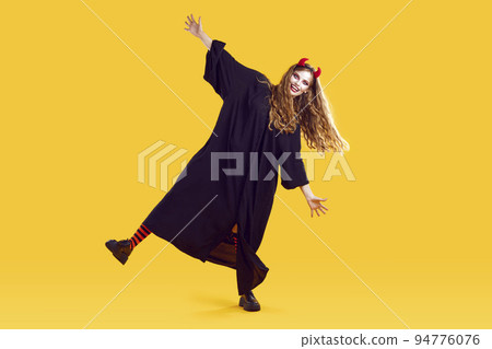 Funky woman in halloween costume, terrifying makeup, red devil horns dancing on yellow background. Funky woman in halloween costume, terrifying makeup, red devil horns dancing on yellow background. 94776076