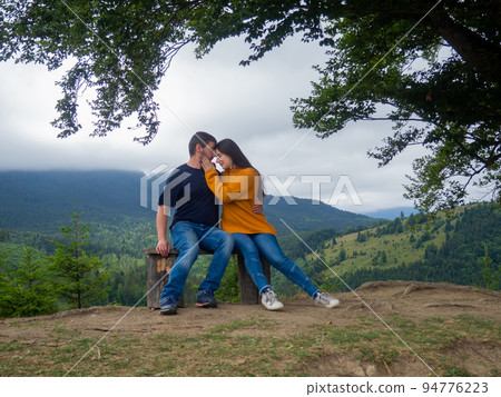 Couple in casual clothes sit under large tree with forest background 94776223