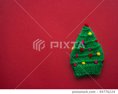 Green knitted hat in the form of a Christmas tree on a red background Green knitted hat in the form of a Christmas tree on a red background 94776224