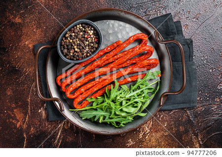 Dry smoked Kabanos or cabanossi traditional Polish thin sausages on a steel tray. Dark background. Top view Dry smoked Kabanos or cabanossi traditional Polish thin sausages on a steel tray. Dark background. Top view 94777206