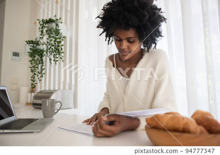 Portrait of young woman working from home reading papers 94777347