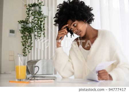 Portrait of young woman working from home checking papers Portrait of young woman working from home checking papers 94777417