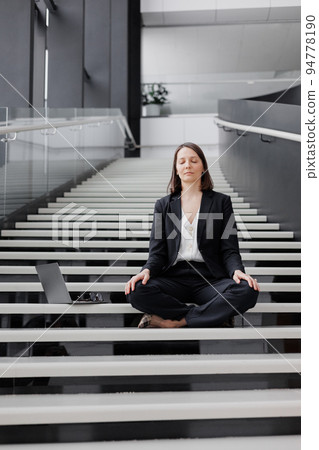 business woman with a laptop in the office of the business center sits on the steps in the lotus position and meditates, relax. business woman with a laptop in the office of the business center sits on the steps in the lotus position and meditates, relax. 94778190