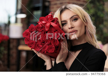 Beautiful woman holding luxury red roses looking at camera, valentines day gift. Attractive blonde girlfriend with flower bouquet in heart shaped box portrait, romance holiday celebration Beautiful woman holding luxury red roses looking at camera, valentines day gift. Attractive blonde girlfriend with flower bouquet in heart shaped box portrait, romance holiday celebration 94779368