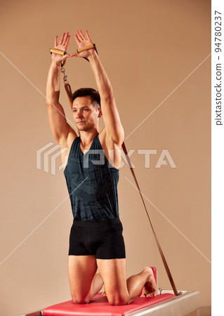 Fit man doing a lunge stretch yoga pilates exercise to strengthen and tone his muscles using a reformer in gym. Health and fitness concept 94780237