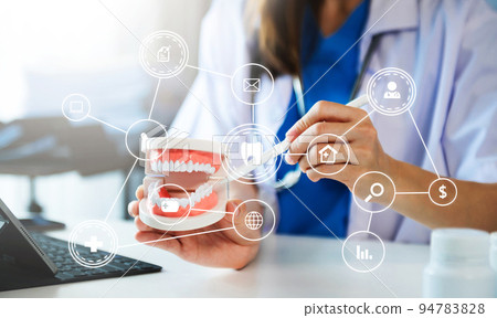 Concentrated dentist sitting at table with jaw samples tooth model and working with tablet and laptop in dental office professional dental clinic. medical doctor working with  VR icon diagram . 94783828