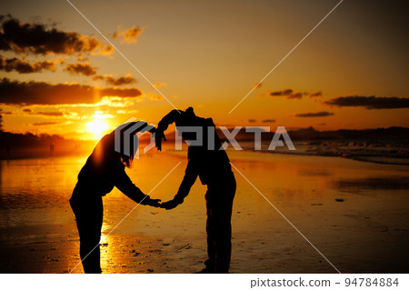 Silhouette of a man and a woman making a heart with their whole body at sunset 94784884