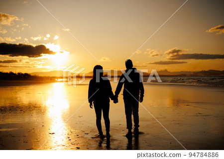 日落時分在沙灘上行走的男人和女人的背影 日落時分在沙灘上行走的男人和女人的背影 94784886