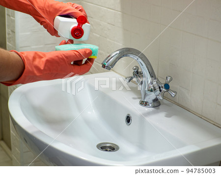 Person hand holding a detergent in white bottle for cleaning bathroom sink 94785003