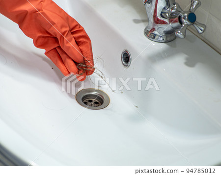 Hand in orange gloves holds many hair loss on filter in washbasin while cleaning Hand in orange gloves holds many hair loss on filter in washbasin while cleaning 94785012