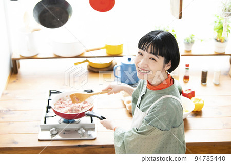 A young woman cooking, looking at the camera, bird's-eye view 94785440
