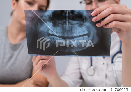 A woman doctor and a patient at the reception are discussing an x-ray of the jaw. 94786025