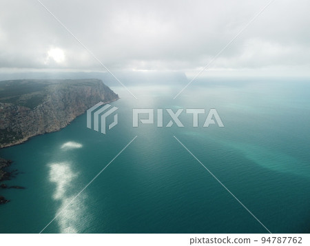 Aerial view from above on calm azure sea and volcanic rocky shores. Small waves on water surface in motion blur. Nature summer ocean sea beach background. Nobody. Holiday, vacation and travel concept 94787762