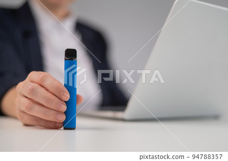 Business woman holding disposable vape while sitting at laptop.  94788357