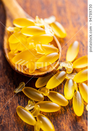 Fish oil capsules in spoon. Yellow omega 3 pills on wooden table. 94789730