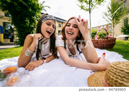 Two women having picnic together, laying on the park lawn Two women having picnic together, laying on the park lawn 94789905