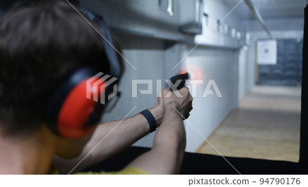 Shooter man holding gun in hand and shooting at a target rear view 94790176