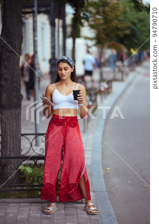 Woman in the street drinking morning coffee and use smartphone. Woman in the street drinking morning coffee and use smartphone. 94790710